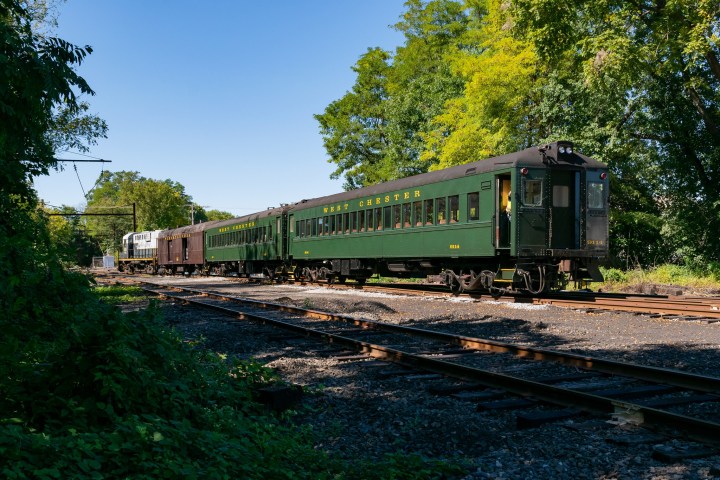 Green vintage train on railway with trees in the background on a sunny day.
