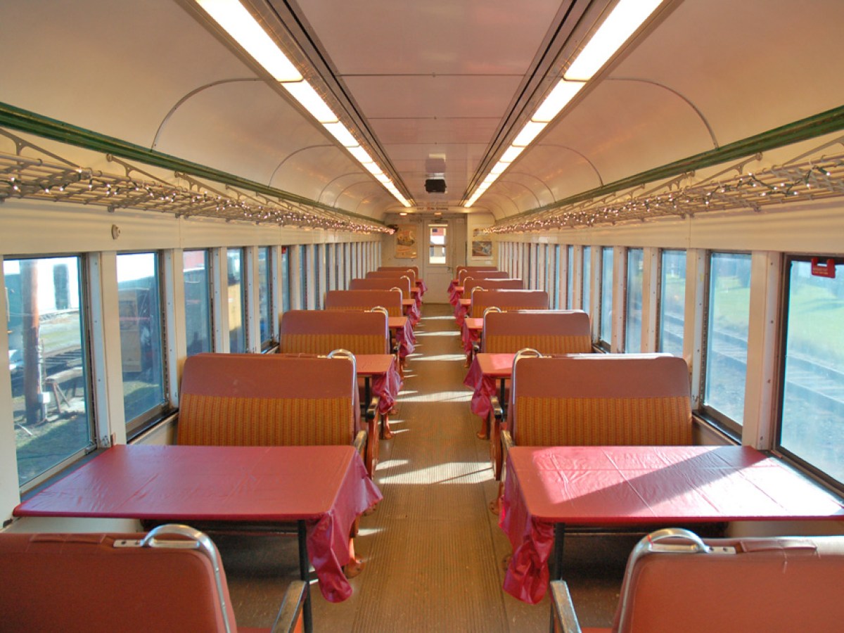 Interior of a vintage train dining car with rows of red-tabled booths.