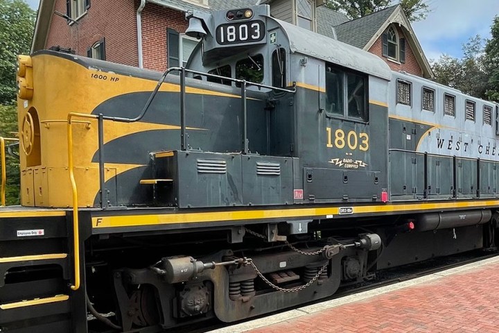 Yellow and gray locomotive engine number 1803 near a brick building.