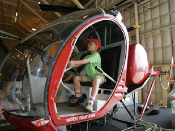 Child in red hat sitting in helicopter cockpit inside hangar.
