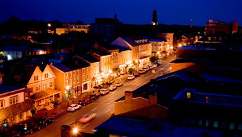 Night view of a small town street with illuminated buildings and parked cars.