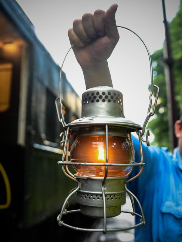 Person holding a lit lantern next to a train car.
