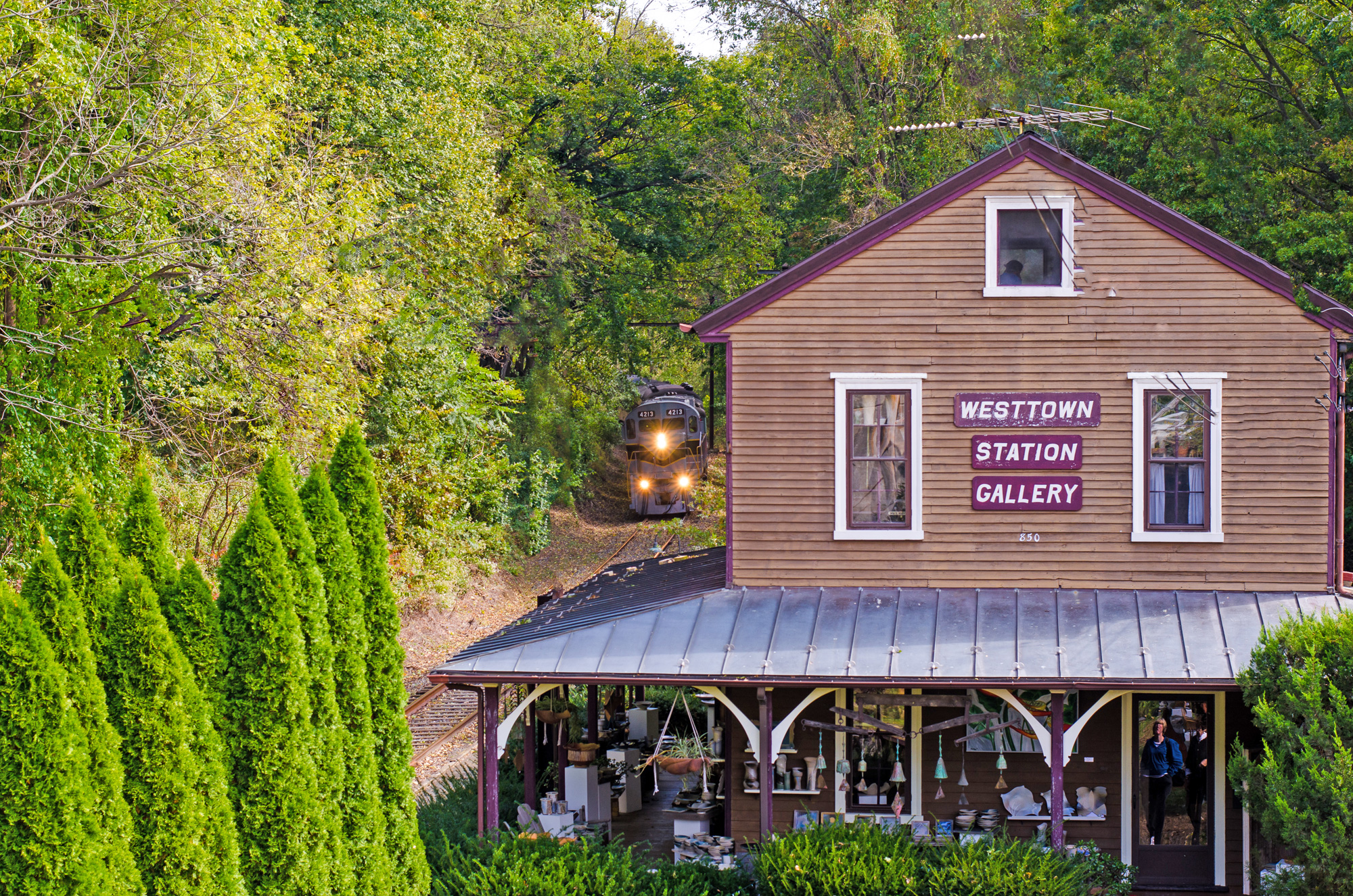 Train approaching Westtown Station Gallery, surrounded by greenery.