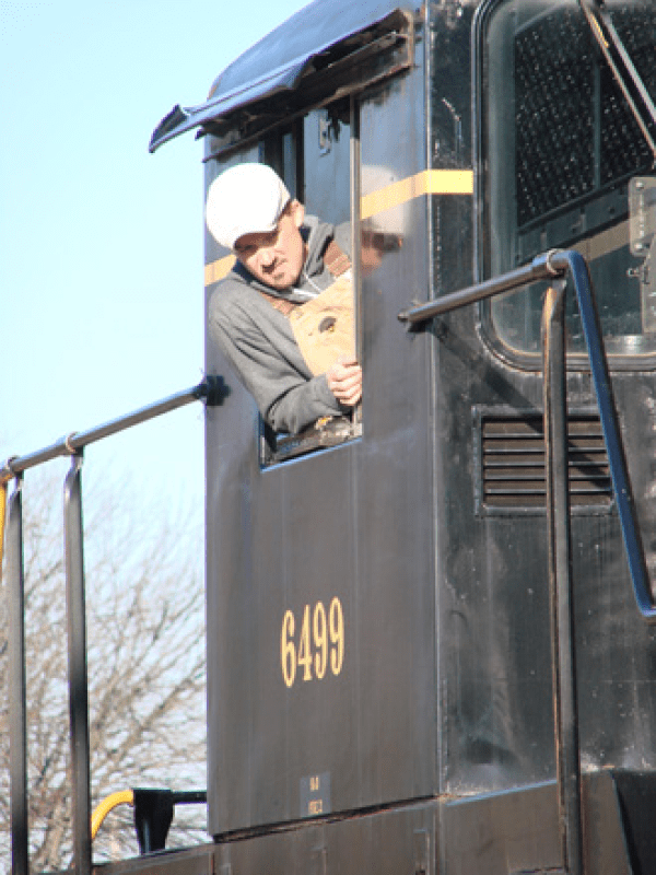 Person in a cap peering out of a black locomotive cabin with number 6499.