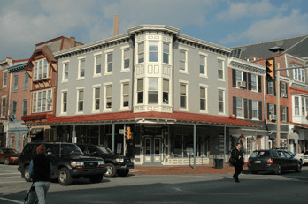 Three-story historic building on a street corner with pedestrians and cars.