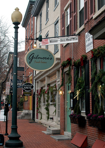Street with brick buildings, festive garlands, and various store signs.