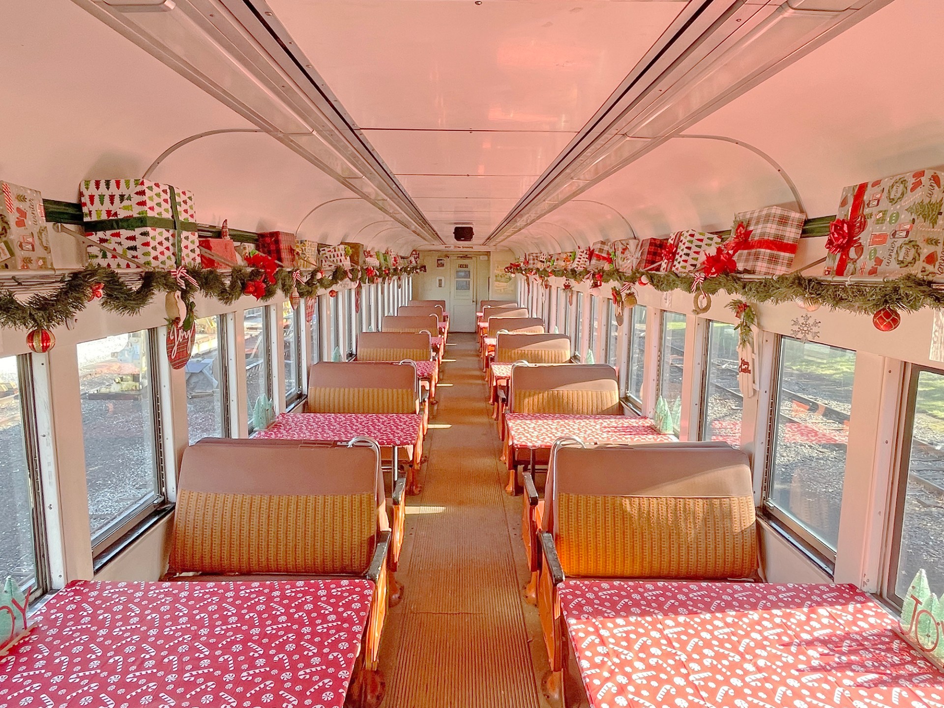 Decorated train car with Christmas garlands and gift-wrapped boxes on shelves.
