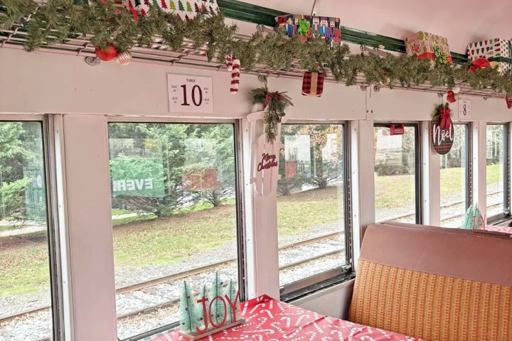 Festively decorated train dining car with red tablecloth and greenery.