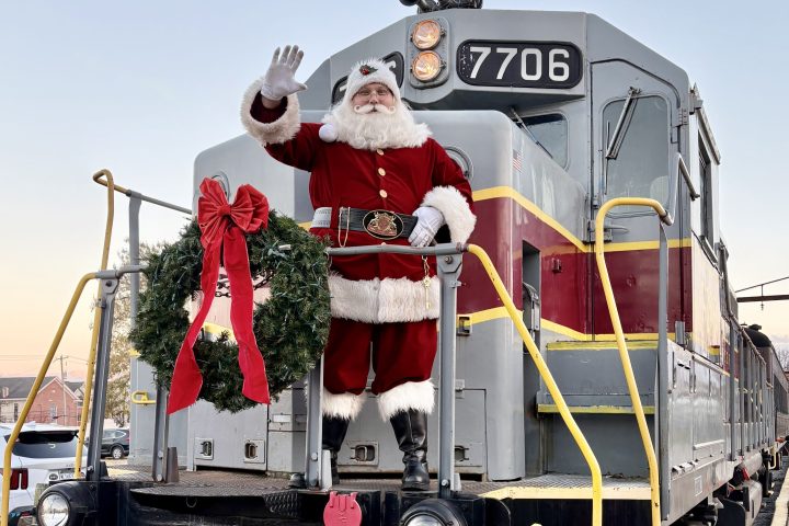Santa waving from locomotive engine adorned with wreath and red bow.