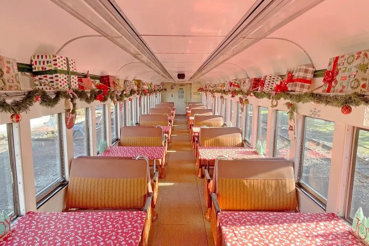 Festive train interior with gift boxes and garlands on shelves.